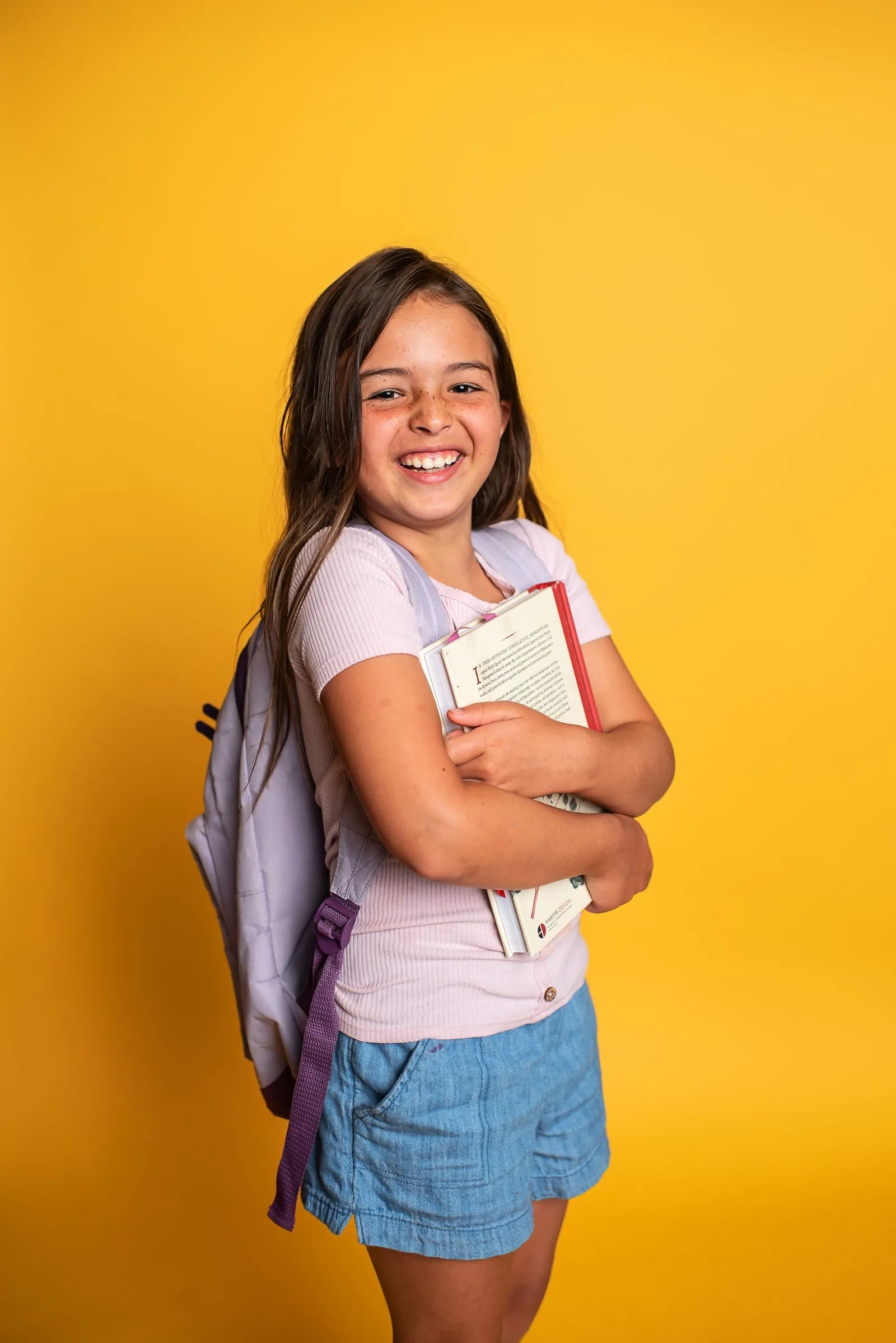 Aluna sorridente segurando livros com mochila nas costas
