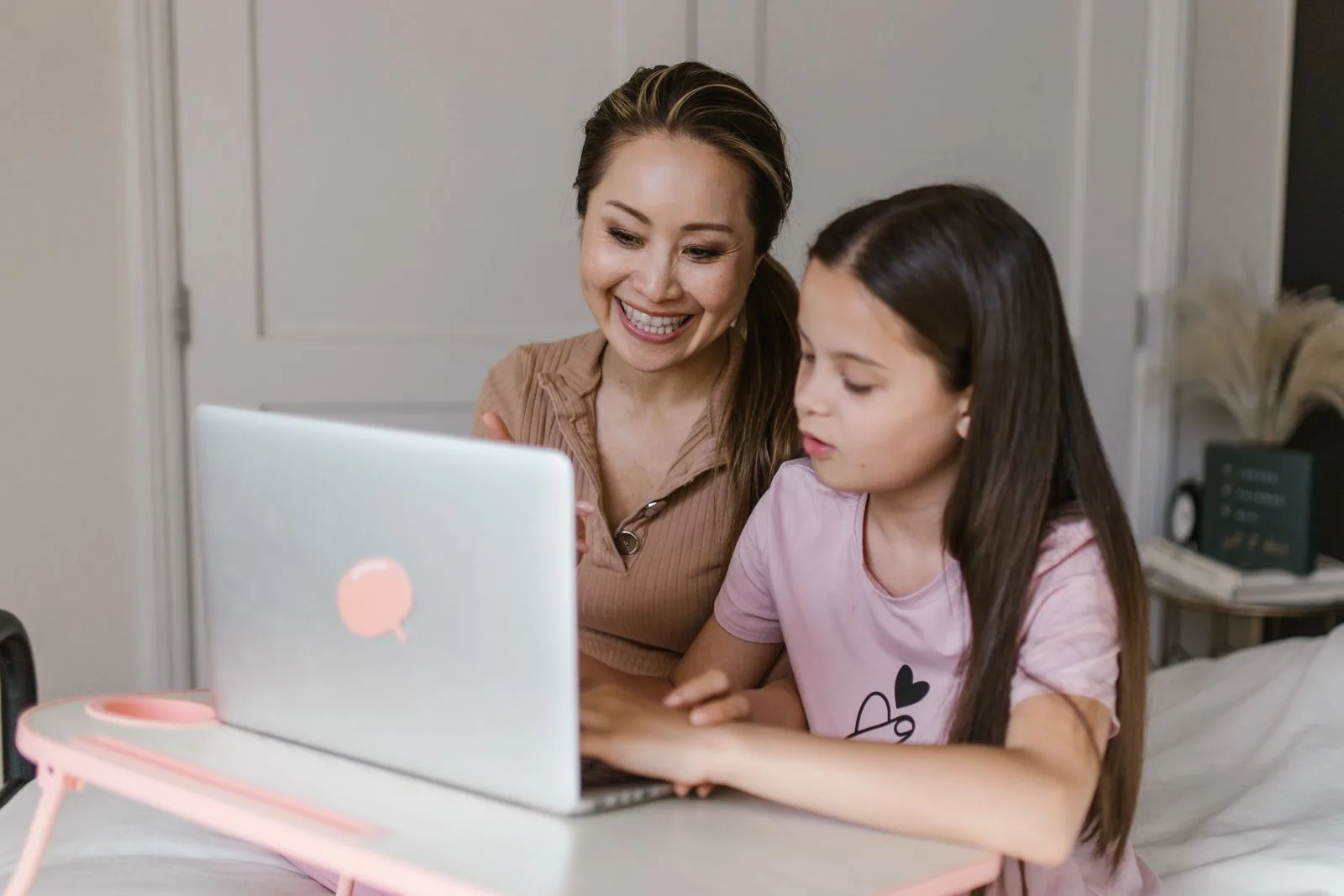 Mãe e filha sorrindo enquanto usam o notebook em casa