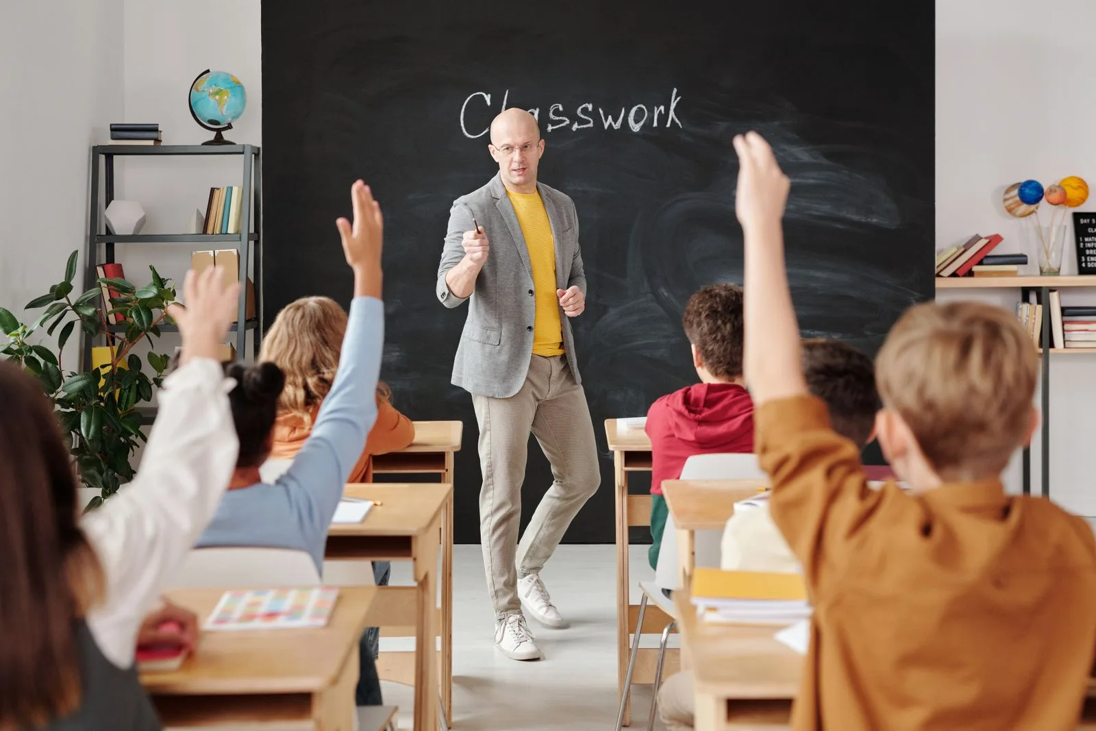 Professor em sala de aula com alunos de mãos levantadas